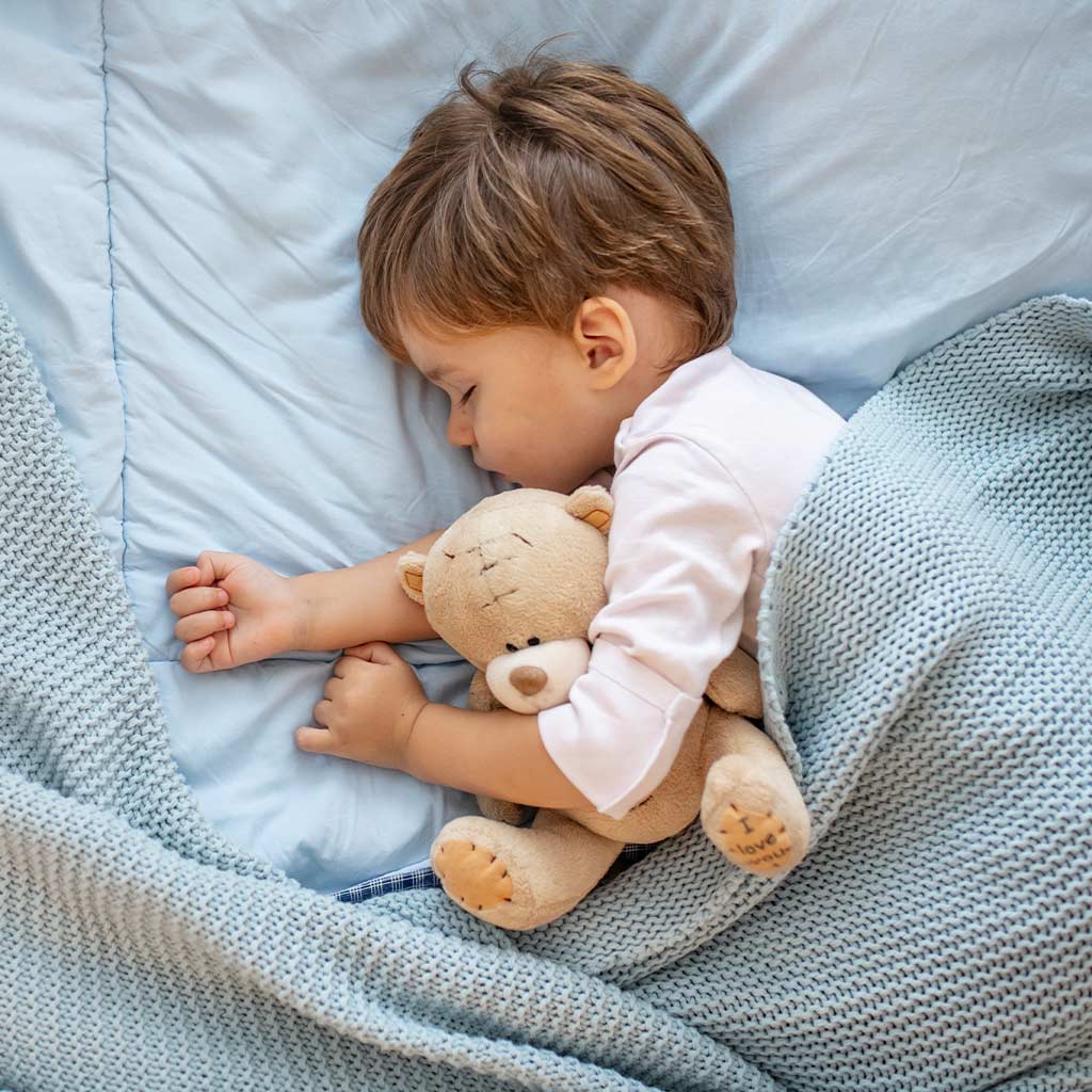 Kleinkind-schläft-friedlich-mit-Teddybär-im-Arm-in-blauer-Wolldecke